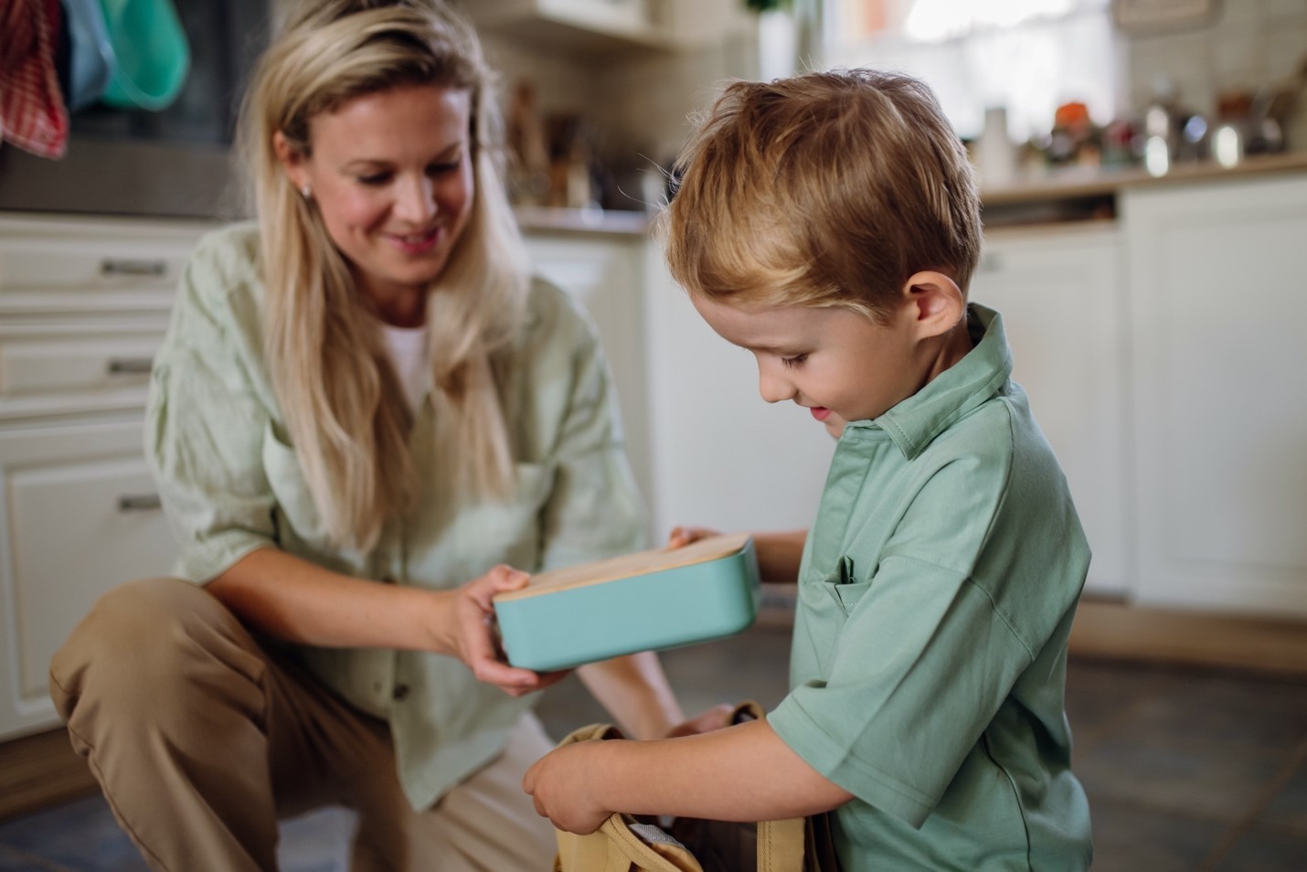 Mom packing a healthy lunch into her son's lunchbox and placing it in his school bag.