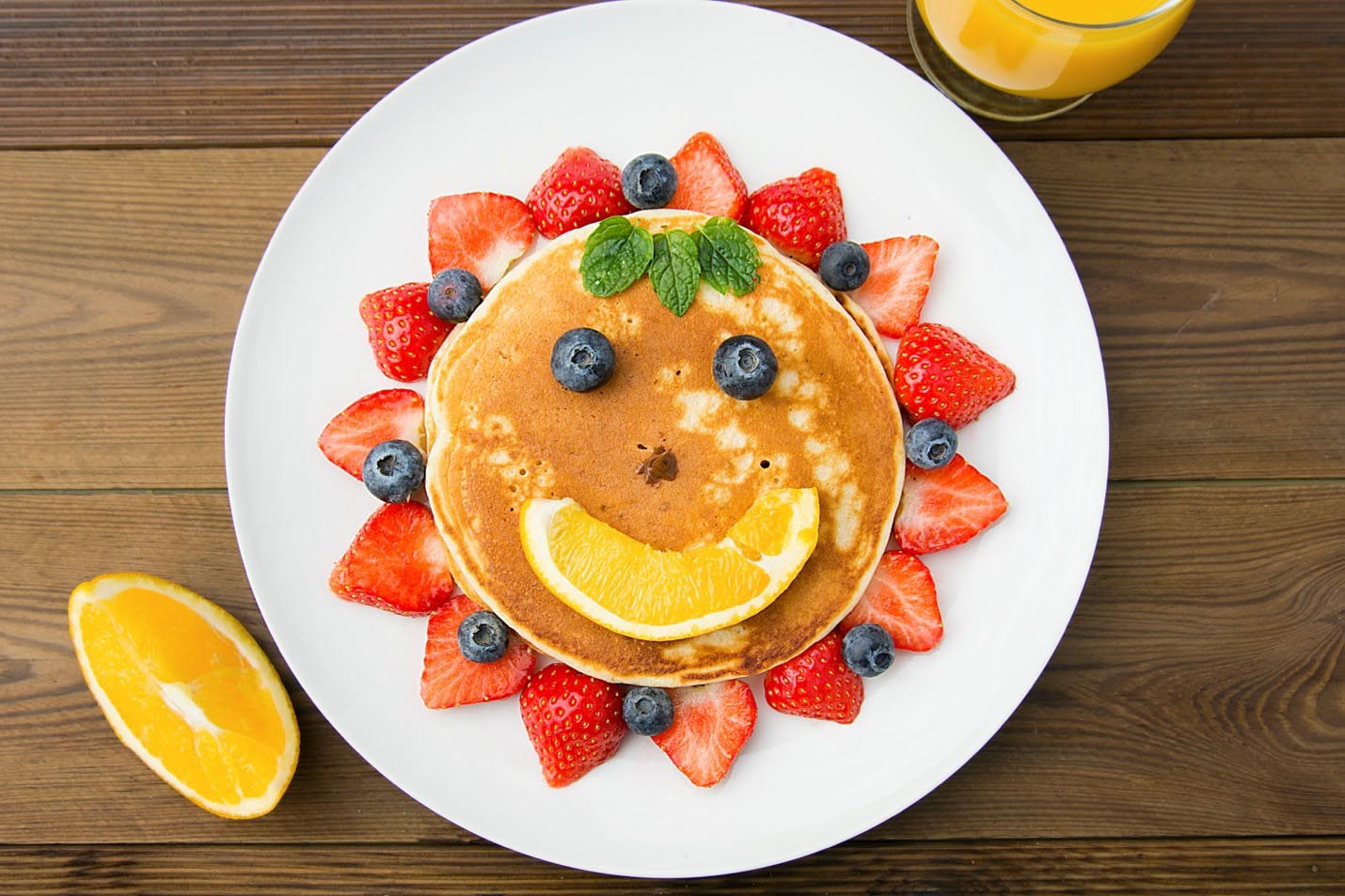 A cheerful breakfast for kids featuring a pancake arranged as a sun, with fresh blueberries and strawberries as toppings.